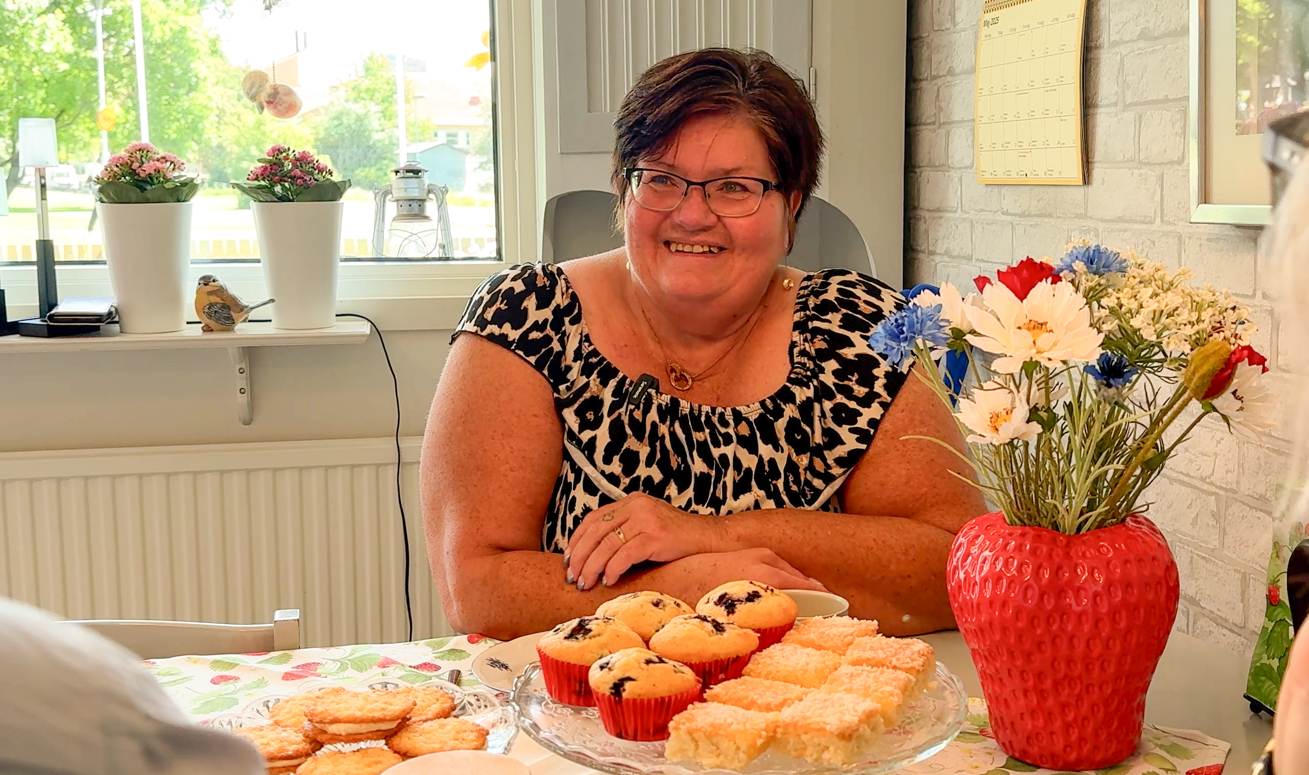 Kvinna sitter vid köksbord med kakor framför sig.