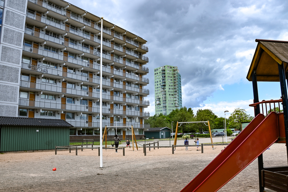 En lekplats med rutschkana och gungor och en fastighet i bakgrunden